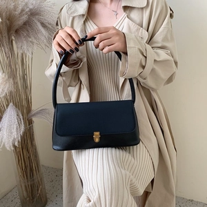 Close-up of black leather handbag with a rectangular gold buckle on beige trench coat
