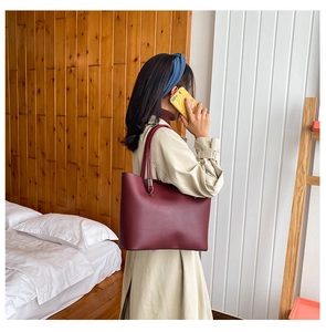 Detail of burgundy matte leather tote bag worn as an underarm shoulder bag on a model