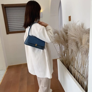 Dark blue leather baguette bag shown on shoulder in a minimalist indoor setting