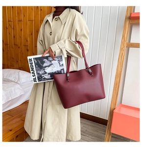 Detail view of large burgundy tote bag with leather straps on model in beige trench coat