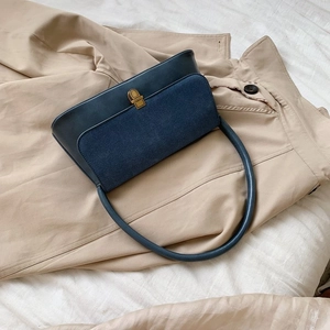 Detail of navy leather and suede shoulder bag with vintage gold buckle on a trench coat