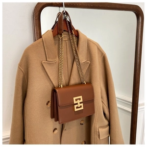 Close-up of brown leather bag with golden geometric lock on camel coat background