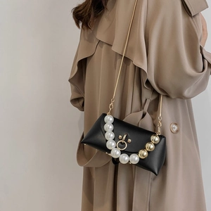 Detail of a black leather crossbody bag featuring a luxury pearl handle and gold chain
