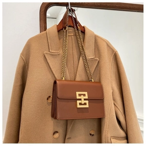 Detail of a brown leather crossbody bag with gold chain strap and geometric metal buckle