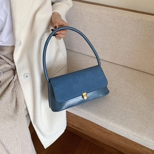 Detail of blue patchwork leather handbag with gold metal lock held by a model