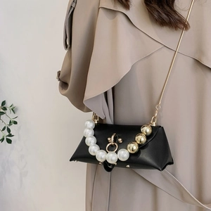 Detail of black leather handbag with faux pearl handle and gold chain strap shown on model