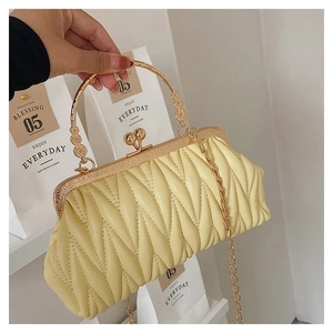 Detail of yellow pleated handbag with gold metal handle and V-shaped quilting texture