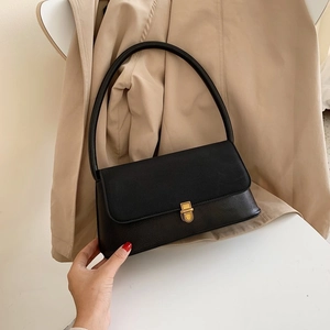 Detail of black faux leather shoulder bag with vintage gold metal clasp on white surface