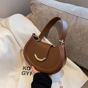 Detail of a brown leather crescent shoulder bag featuring a sleek gold semicircular buckle