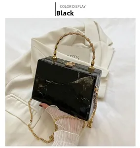 Detail of black marble box bag with golden bamboo handle and lock on white suit background