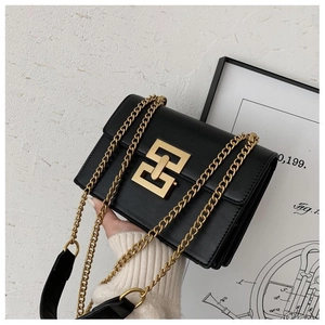 Close-up of black leather crossbody bag with golden geometric lock and chain strap