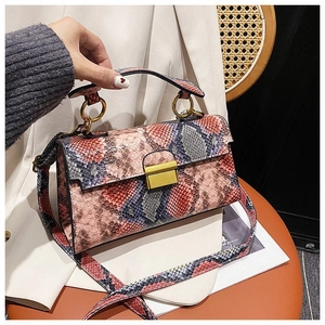 Detail of snake skin pattern cross-body bag with vintage gold hardware on brown stool