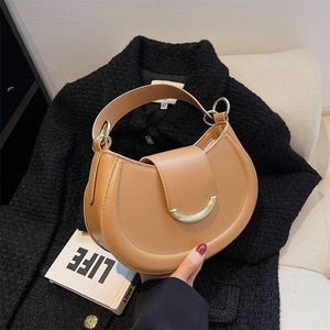 Detail of light caramel crescent saddle bag featuring a gold half-moon metal buckle closure