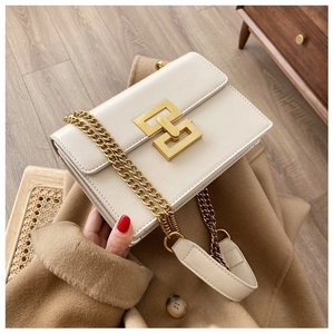 Detail of cream leather flap bag featuring a gold interlocking square buckle and chain strap