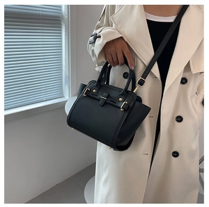 Minimalist black lychee leather kelly handbag with gold buckle shown on a trench coat model