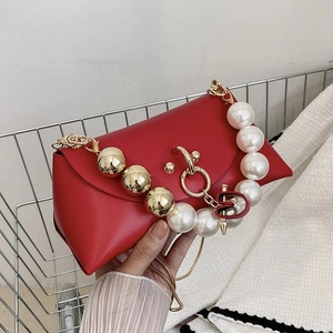 Detail of red faux leather handbag with pearl handle, gold sphere and S-pin ornament