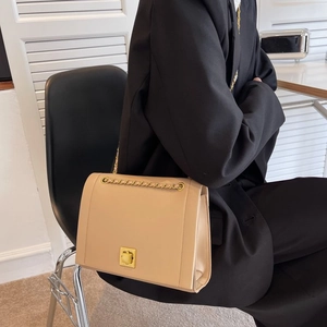 Gros plan d'un sac à rabat en cuir beige avec fermoir doré porté sur un blazer noir