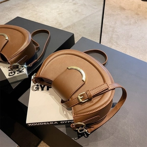 Detail of a brown leather saddle bag with a golden metal buckle on a white book
