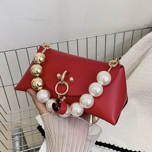 Detail of red matte leather handbag featuring large pearls, gold chain and heart charm