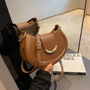Macro view of brown leather saddle bag featuring a distinctive gold crescent buckle closure