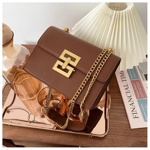 Detailed close-up of brown leather crossbody bag featuring large gold geometric buckle