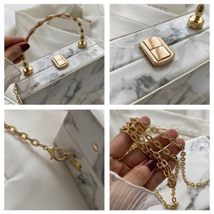 Detail of marble texture clutch with golden bamboo handle and metallic chain strap