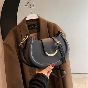Detail of black leather saddle bag with golden crescent buckle and adjustable strap