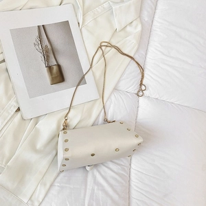 Detailed view of cream white handbag with gold studs and snake chain strap on soft bedding
