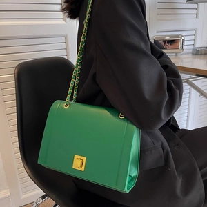 Détail d'un sac à chaîne vert émeraude avec fermoir doré sur une veste de costume noire