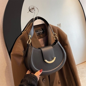 Detail of black leather hobo bag with gold arc buckle and chain strap on a blazer