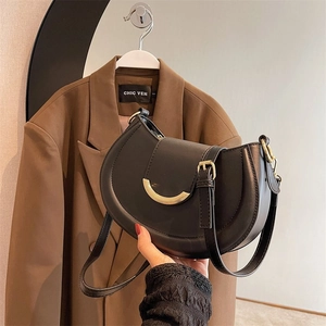 Close-up of black leather saddle bag with vintage gold metal buckle and shoulder strap