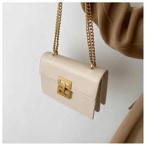 Detail of cream flap crossbody bag featuring gold geometric lock and metal chain straps