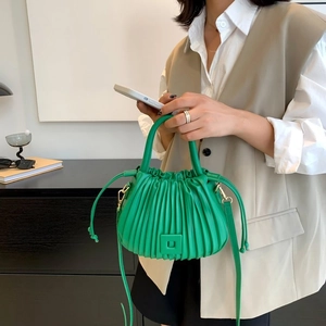 Fashionable green pleated bucket bag with top handle and drawstring closure shown on model