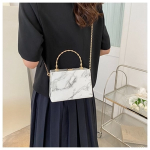 Detail of marble pattern box bag with gold bamboo handle and chain strap on a model