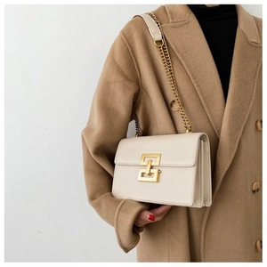 Detail of cream leather crossbody bag featuring gold geometric clasp and chain strap