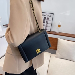 Détail d'un sac bandoulière en cuir noir mat avec fermoir rotatif doré pour femme