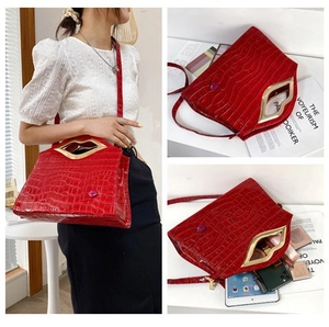 Détail du sac à main rouge motif crocodile avec poignée métallique dorée en forme de lèvres