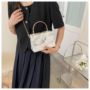 Detail of marble texture clutch bag with golden bamboo handle and metal chain strap