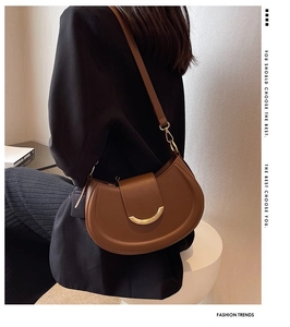 Detail of a brown leather saddle bag with a golden U-shaped buckle and adjustable strap
