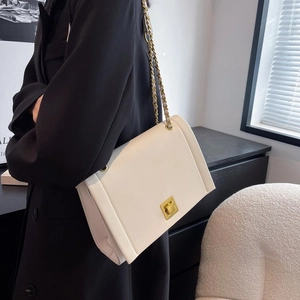 Détail d'un sac à bandoulière blanc avec fermoir doré et chaîne porté par un mannequin
