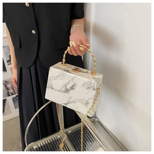 Detail of marble acrylic box bag with golden bamboo handle and metallic chain strap