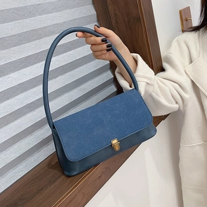 Navy blue baguette shoulder bag with gold clasp and suede texture shown by model