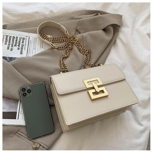 Detail of beige leather crossbody bag with gold buckle next to a phone for size scale