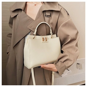Dettaglio borsa in pelle crema con texture litchi e chiusura a girello dorata su trench