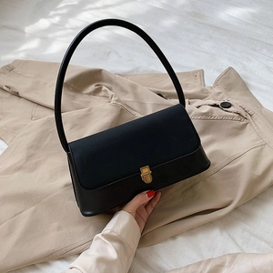 Minimalist black rectangular handbag with gold clasp on a beige trench coat background