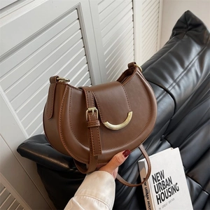 Detailed view of brown saddle bag with golden crescent buckle and adjustable strap