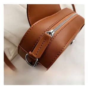 Close-up of smooth silver zipper and stitching on brown leather crossbody bag