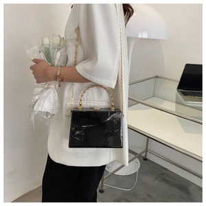 Detail of black marble acrylic clutch bag with golden bamboo handle and chain strap