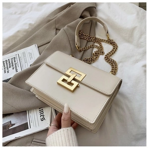 Detail of a chic cream flap bag showing a gold geometric buckle and chain strap