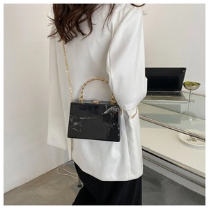 Detail of black marble box bag featuring gold bamboo handle and metallic chain strap